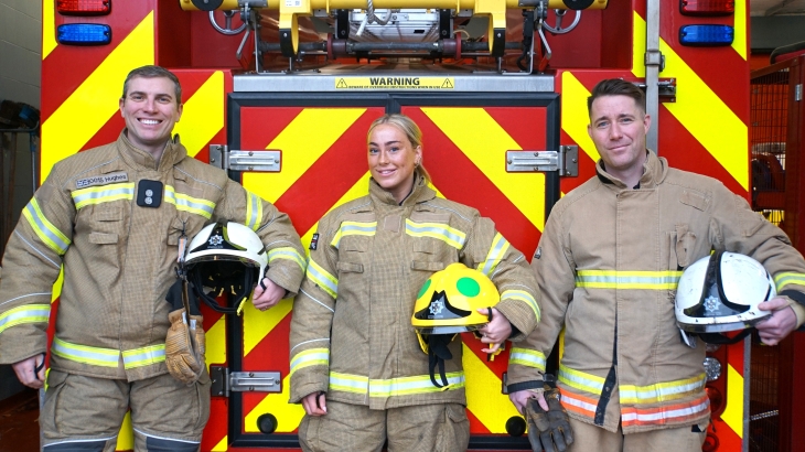 Three on-call firefighters holding helmets in front of fire engine. 