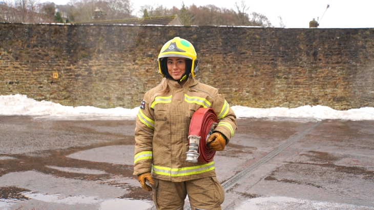 Mya Malthouse is an on-call firefighter in Durham. She is pictured in fire kit carrying a hose.