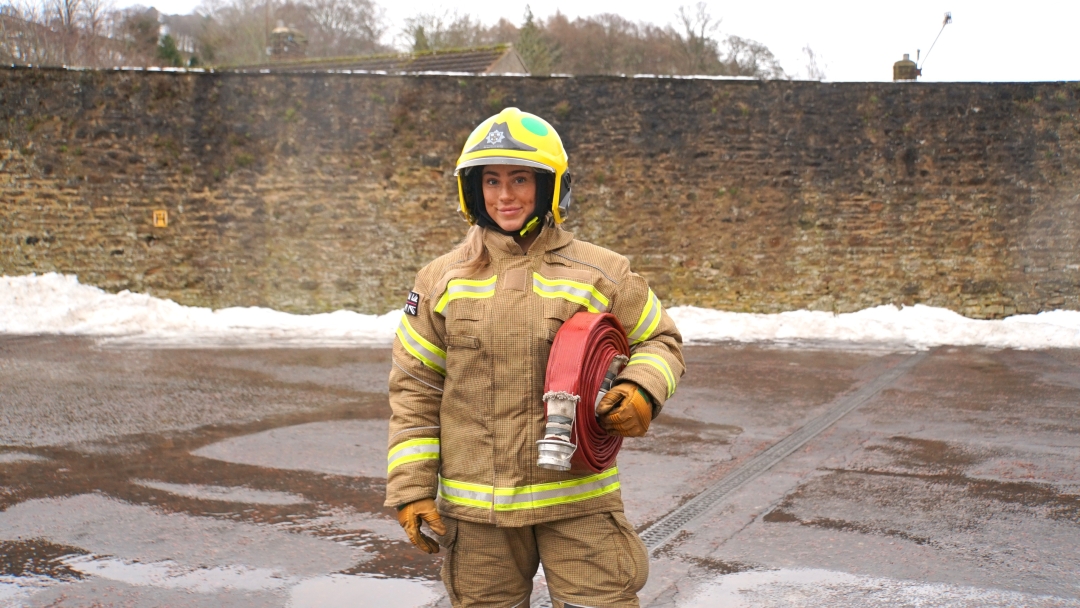 Mya Malthouse is an on-call firefighter in Durham. She is pictured in fire kit carrying a hose.