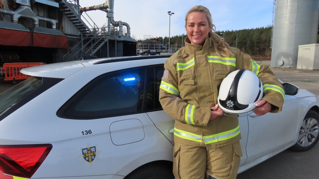 Station Manager Becky Brown wearing fire kit and standing in front of her white car. 